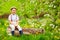 Cute happy boy sitting on wooden stump in spring garden