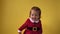 Cute Happy Cheerful Chubby Toddler Baby Girl in Santa Suit Looking On Camera At Yellow Background. Child Playing Scene