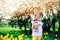 Cute happy child girl holding teddy bear on spring walk with yellow tulips on background