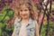 Cute happy child girl in jeans vest enjoying spring near blooming crab apple tree in country garden