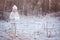 Cute happy child girl in white outfit walking in frozen winter forest