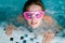 Cute happy girl in pink goggles mask in the swimming pool