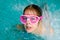 Cute happy girl in pink goggles mask in the swimming pool