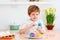 Cute happy kid, boy painting easter eggs at the kitchen desk