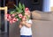 Cute happy little boy holding bouquet of red tulips in front of his face greeting mother or sister or grandmother at home. Mothers