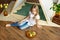 Cute happy little girl with blond hair in a white shirt and blue jeans dreams sitting on the floor near the tent.