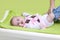 Cute happy little girl getting dressed. Mother dressing her baby on changing pad. Infant baby with pink sweater.