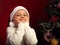 Cute happy smiling kid girl in fur santa claus hat near the Christmas holiday tree thinking about the gift with grimacing face