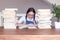 Cute happy smiling tween girl in glasses studying reading book sitting a table with pile of books at home.