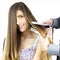 Cute happy woman getting long hair straightened by hairstylist in studio closeup