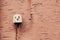 Cute head of character made from the electricity cover on red wall - street art