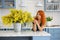 Cute housewife girl in the kitchen where there is a big bouquet of yellow mimosa. Spring. Home comfort