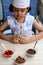 Cute Indian chef girl preparing sundae dish as a part of non fire cooking which includes vanilla ice cream, brownie, coco powder,