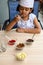 Cute Indian chef girl preparing sundae dish as a part of non fire cooking which includes vanilla ice cream, brownie, coco powder,