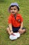 Cute Indian toddler wearing cap, sitting and smiling inside a garden, Pune, Maharashtra