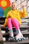 Cute indie girl with roller skates sitting on stairs indoors