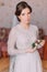 Cute innocent bride at home in white wedding dress, preparations concept. Portrait of tender girl in gown