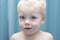 Cute innocent toddler looking at camera. Close-up portrait against blue background