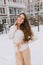 Cute joyful amazing young woman with long brunette hair in white woolen sweater, light skirt walking on street on winter