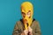 Cute kid covering his face with yellow knitted thief mask and smiling on blue