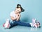 Cute kid girl with funny buns in t-shirt and blue jeans is sitting with roller skates on her feet, nice posing