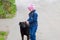 Cute kid girl in a pink hat with pigtails in a blue denim jacket stroking a stray black adult dog outdoors