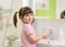 Cute kid girl with ponytail in pink bathrobe washing her hands.