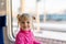 Cute kid girl travelling by raailroad. Child smiling and sitting in train. Wide bright sunny window on background. Copyspace