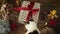 Cute kitten walking at stylish christmas gift with red ribbon on rustic wooden table with festive decorations. Curious cat and xma