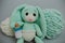 Cute knitted light green bunny with big ears in a white diaper with a knitted white pacifier with two skeins knitting yarn