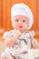 Cute liitle girl in chef`s hat sitting on the kitchen floor soil