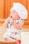 Cute liitle girl in chef`s hat sitting on the kitchen floor soil