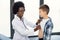 Cute likable Caucasian teen boy and joyful African woman doctor, during doctors checkup. Pediatrist examinates young