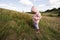 Cute litlle girl walking on autumn hill wearing a pink jacket with hood and rubber boots