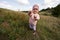 Cute litlle girl walking on autumn hill wearing a pink jacket with hood and rubber boots