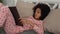 Cute little African American girl enthusiastically reads a book with fairy tales. Teenage girl in pajamas lies on bed in