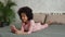 Cute little African American girl sings looking at the smartphone screen and records video. Teenage girl in pajamas lies