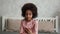 Cute little African American girl sings looking at the smartphone screen and records video. Teenage girl in pajamas sits