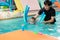 Cute little Asian 2 year old toddler boy child wear swimming goggles learning to swim with pool noodle at indoor pool