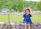 Cute little asian girl wear straw hat sitting on the stone wall against green public garden