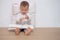 Cute little Asian toddler baby boy child sitting on floor, leaning against pillow, looking at a book, turning the page of a book w