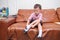 Cute little Asian toddler boy child sitting on sofa in living room concentrate on putting on his own socks