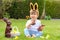 Cute little baby boy with bunny ears eating chocolate Easter bunnies sitting on green grass outside in the spring garden with bask