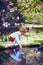 Cute little baby boy puts his hand into the pond water in spring garden