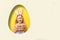 Cute little baby girl with bunny ears holding basket of Easter eggs. A child in a hole in the shape of an egg