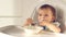 Cute little baby girl eating baby food with spoon. her face is smeared with yoghurt on high chair in home kitchen