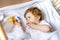 Cute little baby girl holding bottle with formula mild and drinking. Child in baby cot bed before sleeping