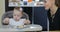 Cute little baby girl sitting in kids chair and sharing food with her mom.