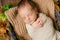 Cute little baby sleeping in a wicker basket of twigs with little orange pumpkins.