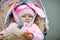 Cute little beautiful baby girl sitting in the pram or stroller on autumn day. Happy smiling child in warm clothes